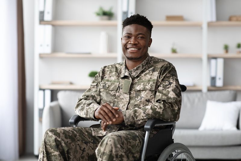 A young soldier in uniform smiles from his wheelchair in a living room.